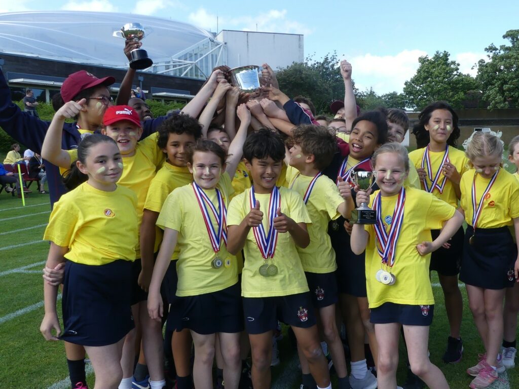 Children in yellow t-shirts lifting trophy at sports day