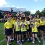 Children in yellow t-shirts lifting trophy at sports day