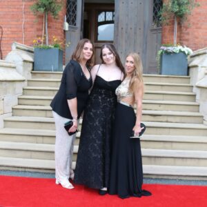Three girls in prom dresses on red carpet