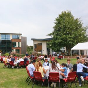 A group of families and students seated around circular tables on a grassy lawn