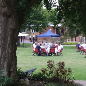 A group of families and students seated around circular tables on a grassy lawn