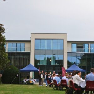 A group of families and students seated around circular tables on a grassy lawn in front of modern building